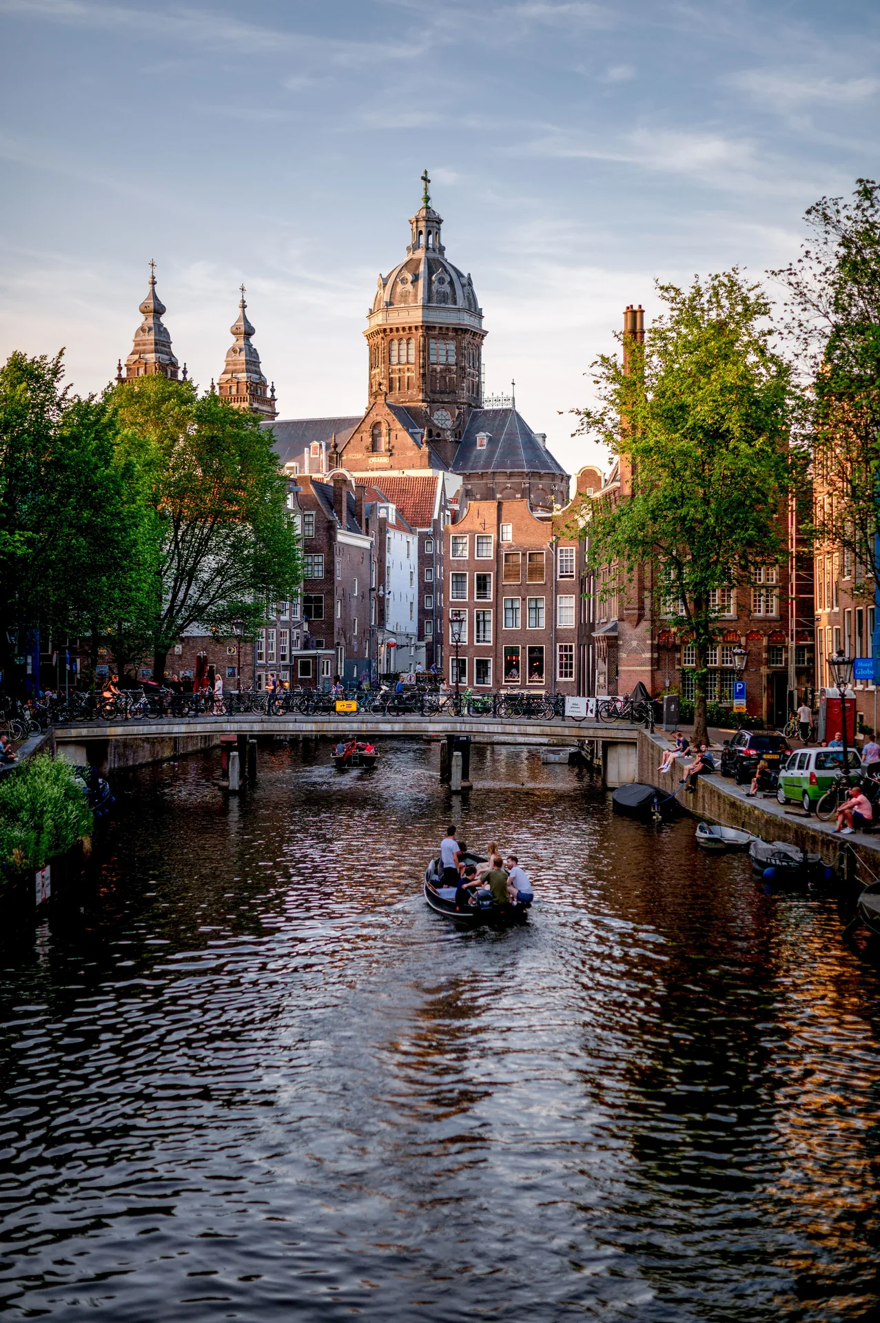 A boat on an Amsterdam canal at sunset, with the dome of the Sint-Nicolaaskerk behind